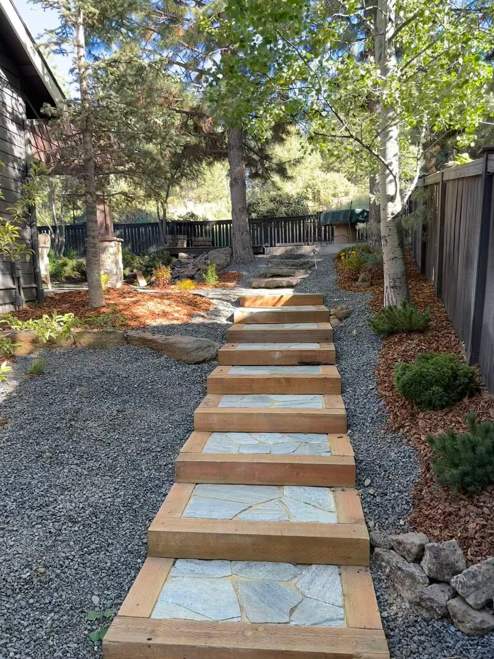A long run of steps up a shaded slope, each tread framed in timber and filled with fitted flagstone, gravel and bark beds on both sides.