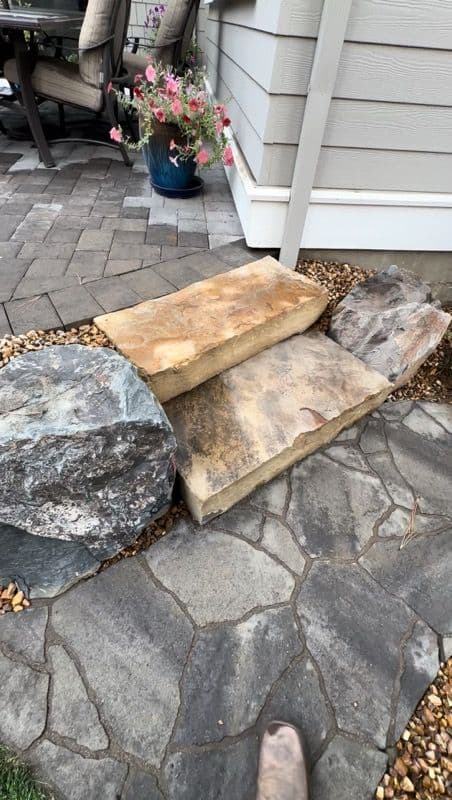 Close view of two sandstone slab steps bedded between a gray boulder and a tan boulder, with pea gravel worked in at the edges.