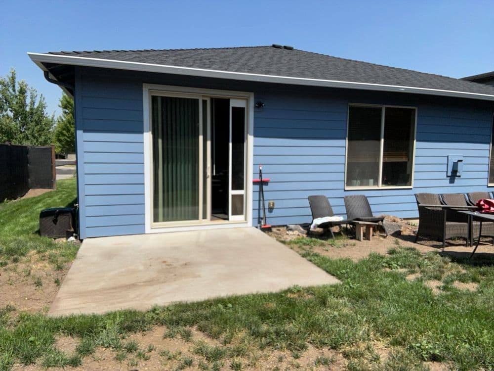Blue house exterior with sliding glass door and patio furniture on a grassy yard.
