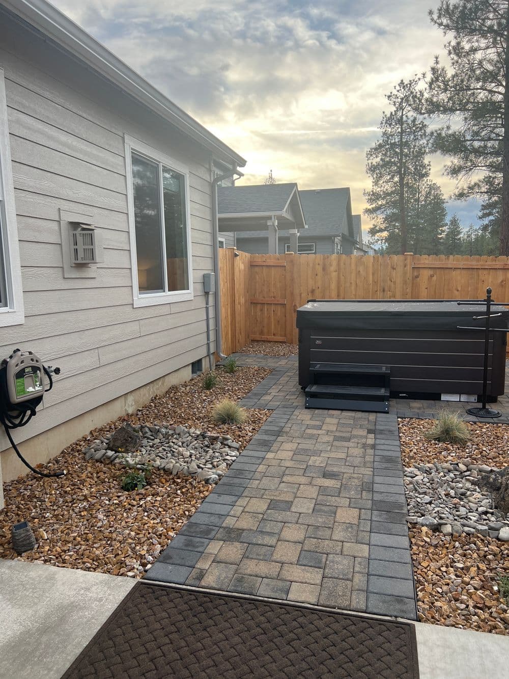 Pathway leading to a hot tub in a landscaped backyard with a wooden fence.