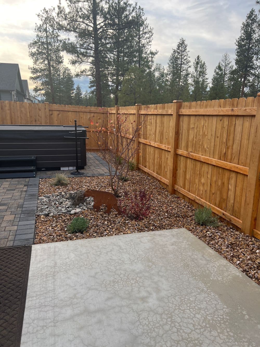 Landscaped patio area with gravel, small shrubs, and a tree surrounded by wooden fencing.