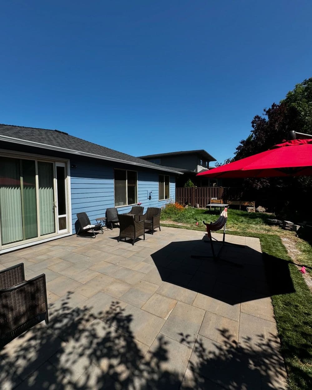 Spacious backyard patio with seating and a red umbrella under a clear blue sky.