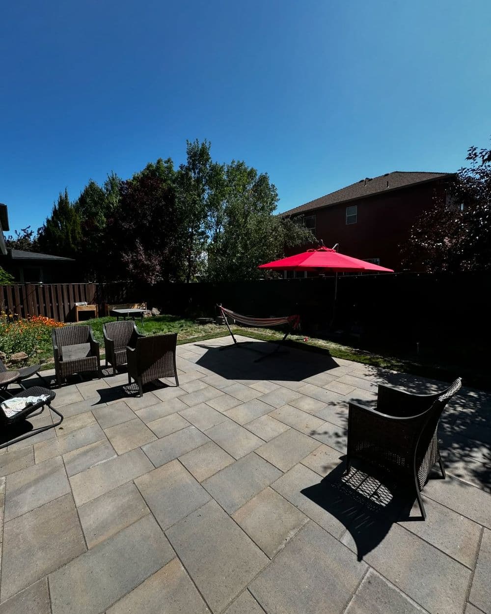 Backyard patio with chairs, hammock, and red umbrella under clear blue sky.