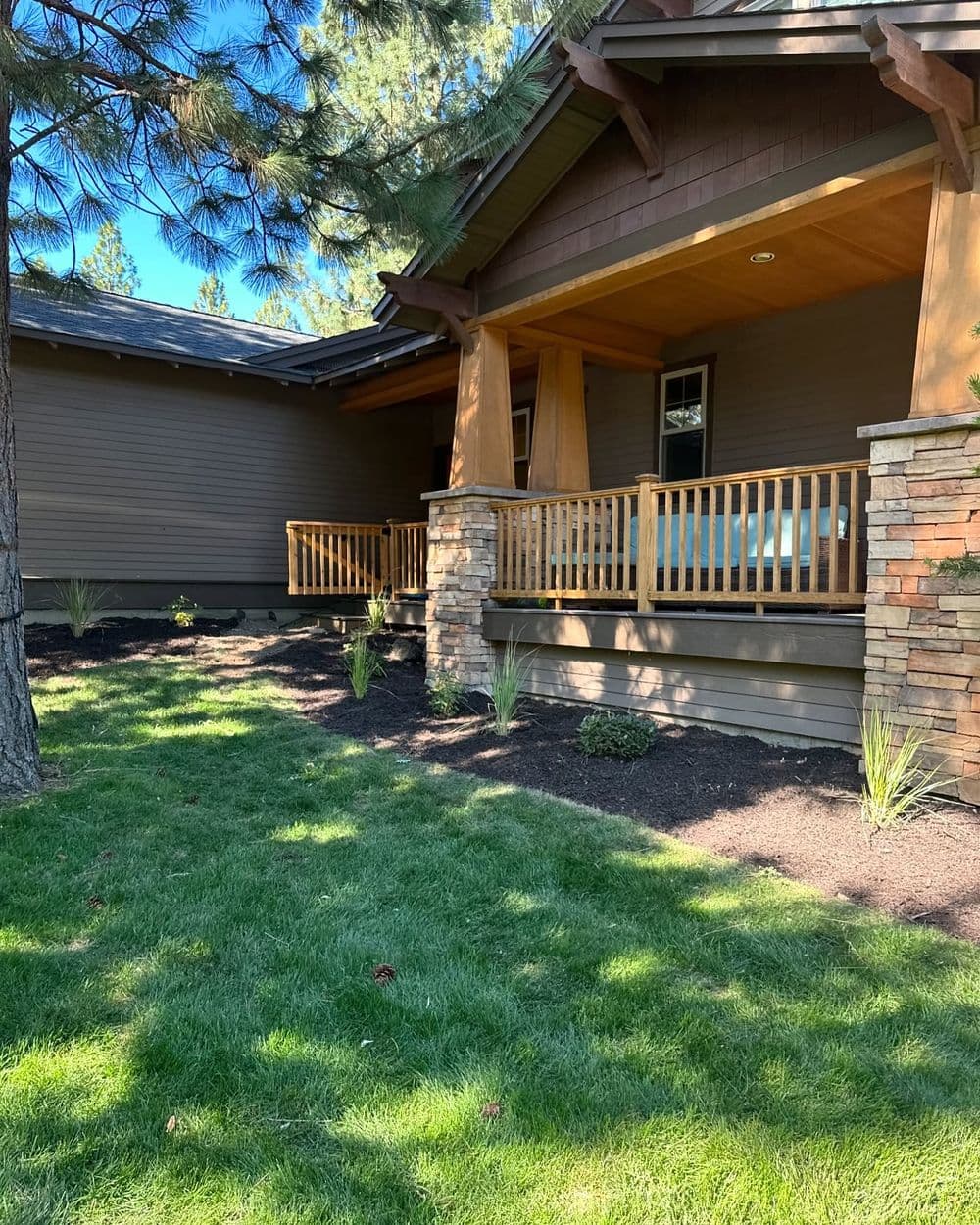 Cozy home exterior with wooden porch, lush green lawn, and landscaped garden area.
