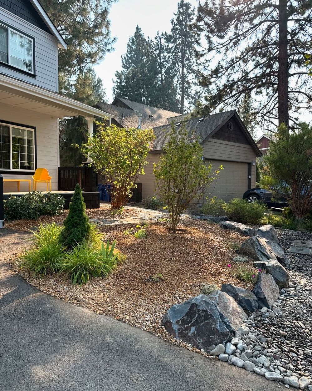 Front yard landscaping with rocks, shrubs, and gravel near a house and garage.