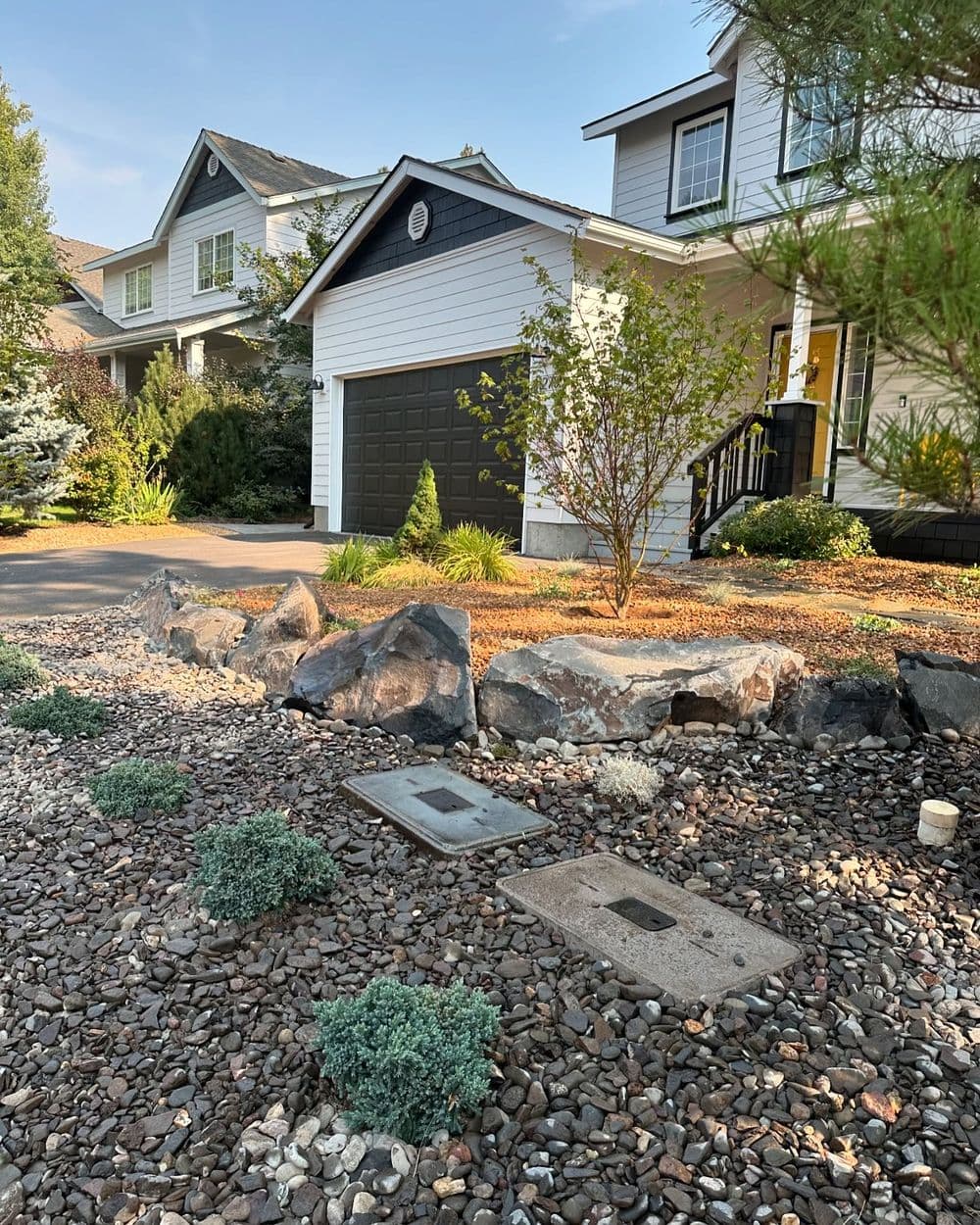 House exterior with landscaped garden featuring rocks and shrubs, driveway, and garage door.