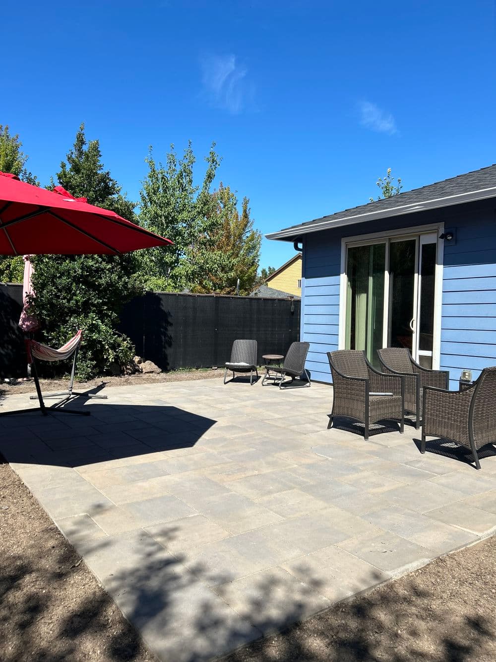 Large-format square paver patio behind a blue house, with an umbrella, hammock and patio chairs on it.